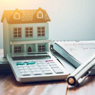 Miniature house model perched on a calculator next to a pen, suggesting real estate calculations or home financing.