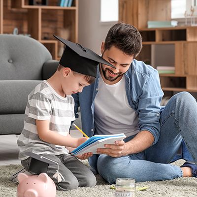 Father and young son sitting on the floor, reading a book together in a living room, focused on the pages with smiles.