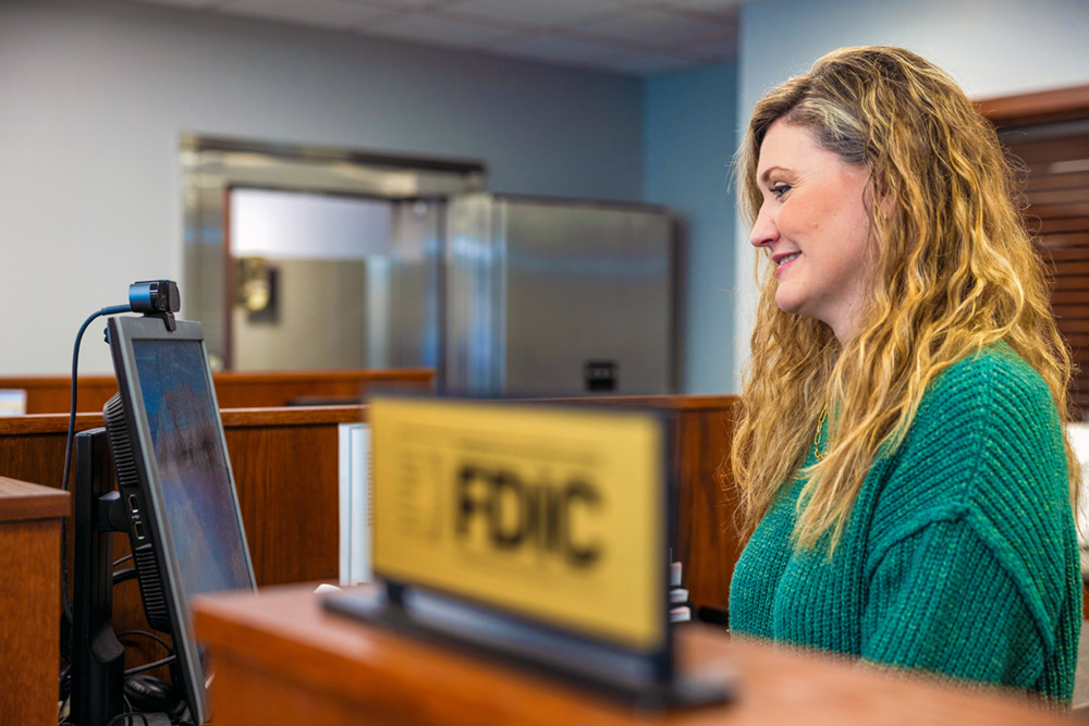 Woman behind teller line, smiling while working on computer